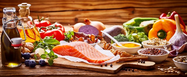 Auf einem Tisch liegen gesunde Lebensmittel wie Fisch, Obst, Gemüse und Öle