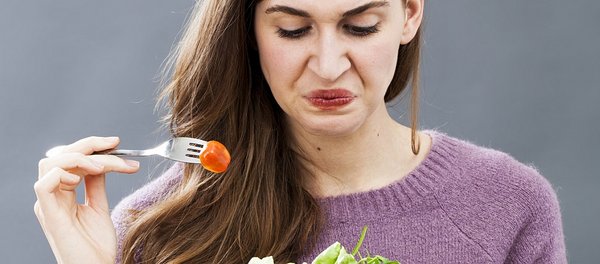 Frau hält Gabel mit Tomate und schaut angewidert auf Salat