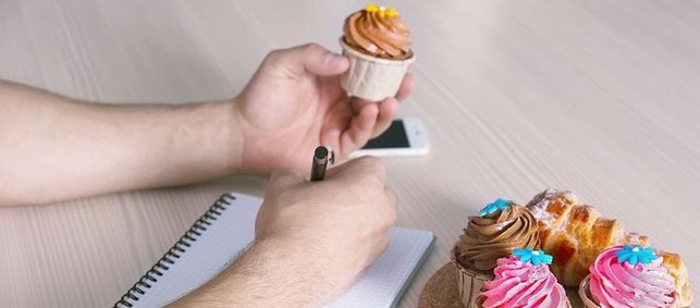Mann hält Cupcake in der Hand und schreibt auf Blatt