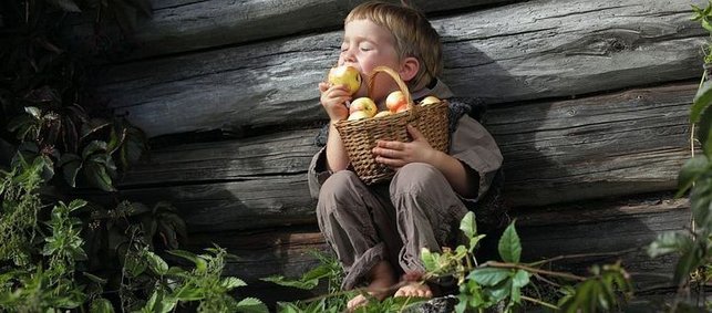 Junge lehnt gehockt an Wand einer Holzhütte und beißt in Apfel