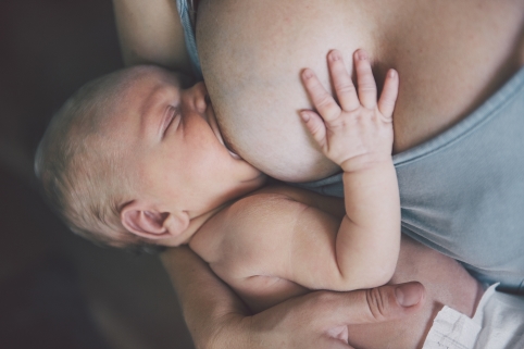 Ein Baby trinkt mit weit geöffnetem Mund an der Brust der Mutter.