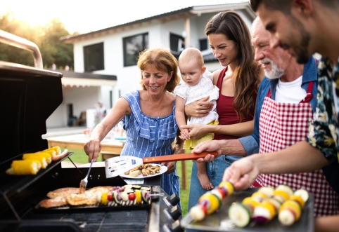 : Eine Familie beim Grillen: Maiskolben werden indirekt gegrillt, Fleisch und Gemüsespieße in einer Schale