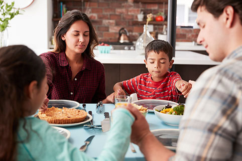 Eine Familie hält sich mit geschlossenen Augen die Hände und betet vor dem Essen.