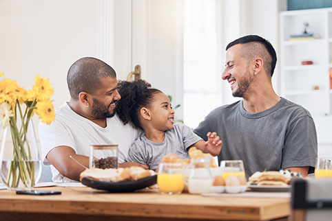 Eine Familie mit zwei Vätern und einer Tochter essen gemeinsam Frühstück.