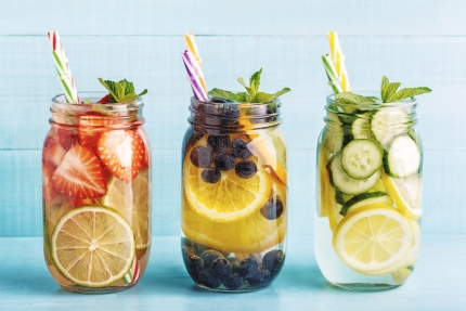 : Drei Gläser Wasser mit jeweils Erdbeeren, Zitronenscheiben, Littenscheiben, ganzen Beeren, Gurkenscheiben, Kräutern. 