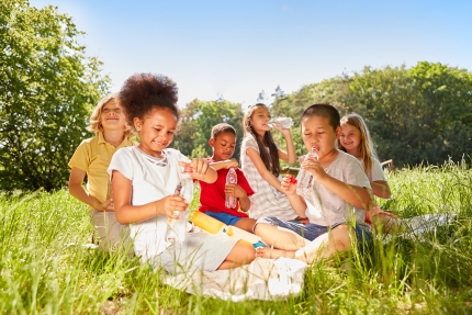 Eine Gruppe von Kindern sitzt auf einer Wiese und sie trinken Wasser.