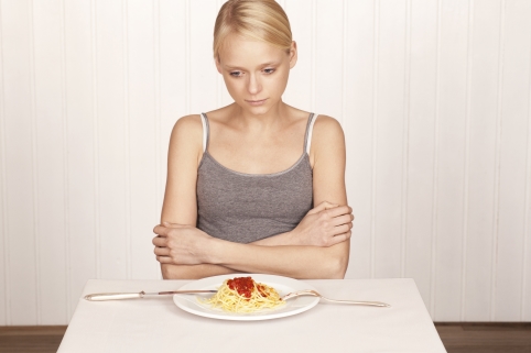Bild: Eine Frau sitzt vor einem Teller und hat keine Lust zu essen.