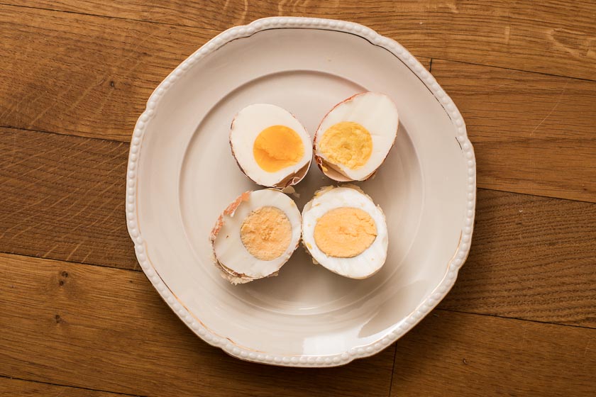 Vier längs aufgeschnittene Eier liegen auf einem Teller, die Dotter pflaumig-weich bis hart.