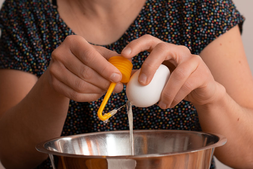 Frau presst Luft mit einem Mini-Blasebalg ins Ei, bis das Eiklar herausläuft.