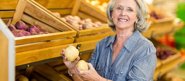 Frau vor Regal mit Kartoffelsorten und hält zwei Kartoffeln in der Hand