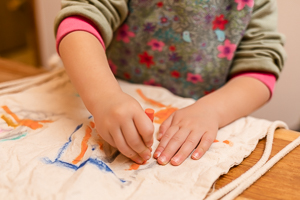 Mädchenhände malen orangefarbene Striche auf einen Leinenbeutel.