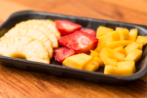 Ananas, Erdbeeren und Mango fertig geschnitten in einer schwarzen Plastikschale.