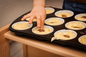Kinderhand drückt Schokoostereier in den Muffinteig.