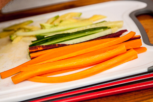 Für Sushi wird das Gemüse in lange, dünne Streifen geschnitten. Hier: Karotten, Gurke und Avokado auf einem weißen Brett.