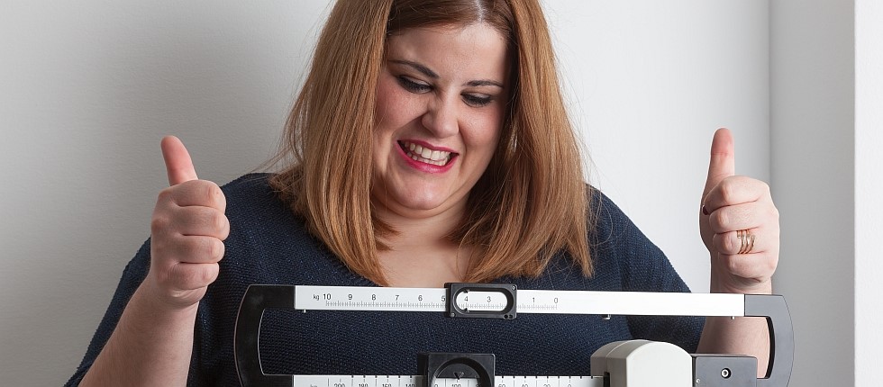 Übergewichtige Frau steht auf Waage und jubelt