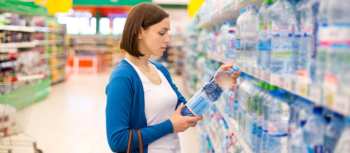 Eine Frau schaut sich das Etikett einer Mineralwasserflasche am Supermarktregal an