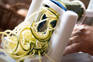 Zucchini wird durch einen Spiralschneider gedreht; heraus kommen lange dünne Nudeln aus Zucchini