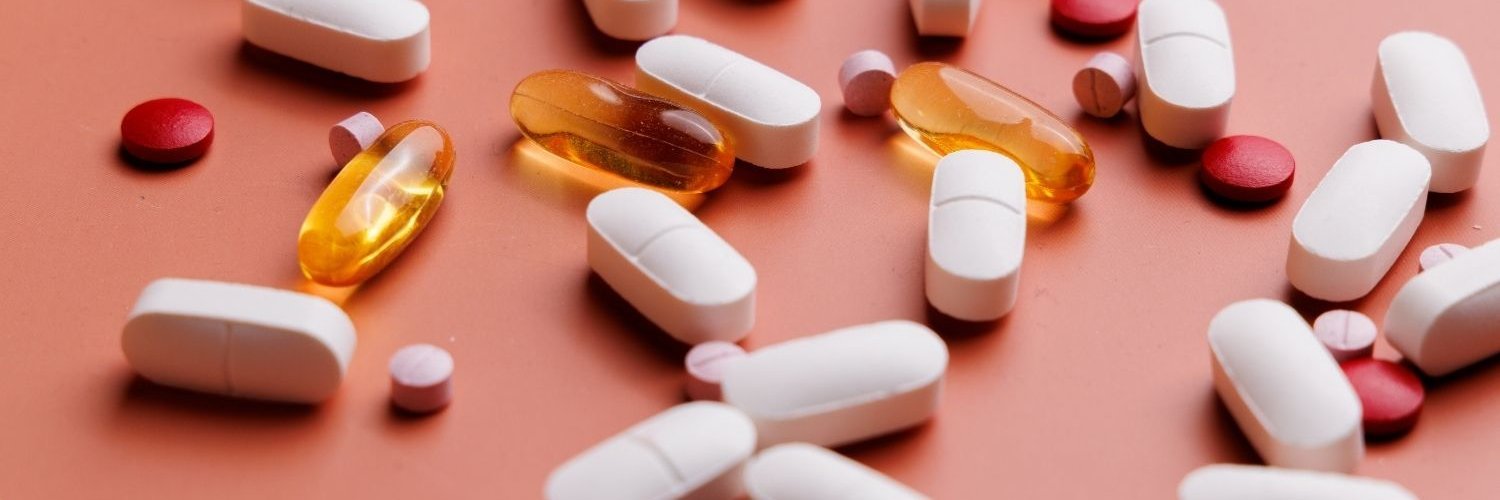 Auf einem altrosa Untergrund liegen verstreut weiße Tabletten, gelbe Kapseln sowie rosa und rote Pillen.