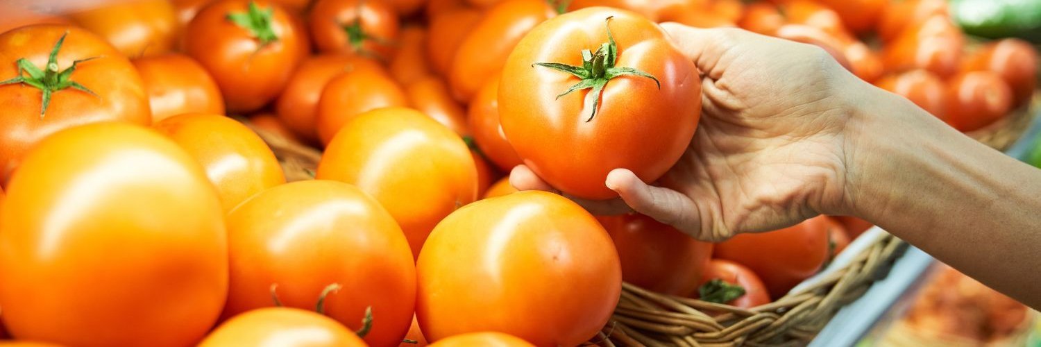 Eine Hand greift eine Tomate aus einem Regal mit Tomaten in Gemüsekisten.