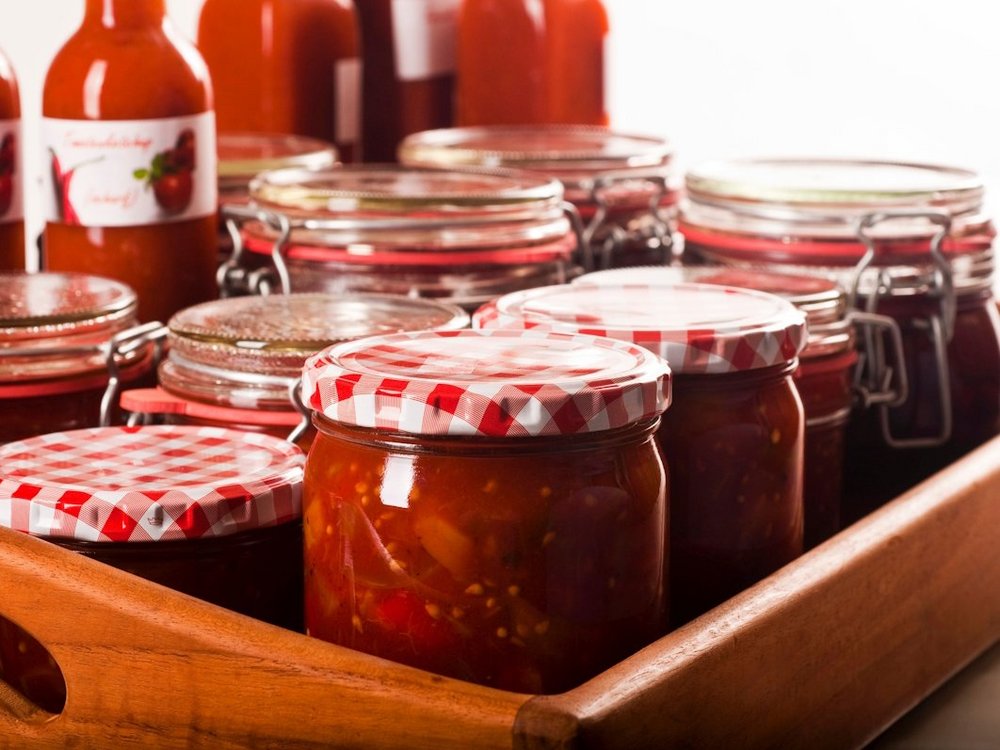 Mehrere Gläser und Flaschen mit eingekochtem Tomatenketchup stehen auf einem Tablett.