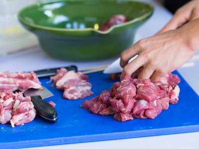 Haende schneiden Fleisch hygienisch auf einem Brettchen.