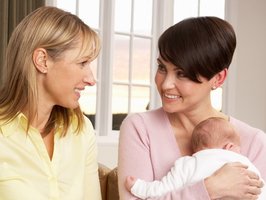 Eine junge Mutter mit ihrem Säugling auf dem Arm unterhält sich mit ihrer Hebamme