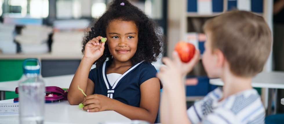 Zwei Kinder in einem Klassenraum zeigen sich gegenseitig eine Traube und einen Apfel