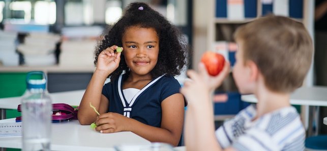 Zwei Kinder in einem Klassenraum zeigen sich gegenseitig eine Traube und einen Apfel