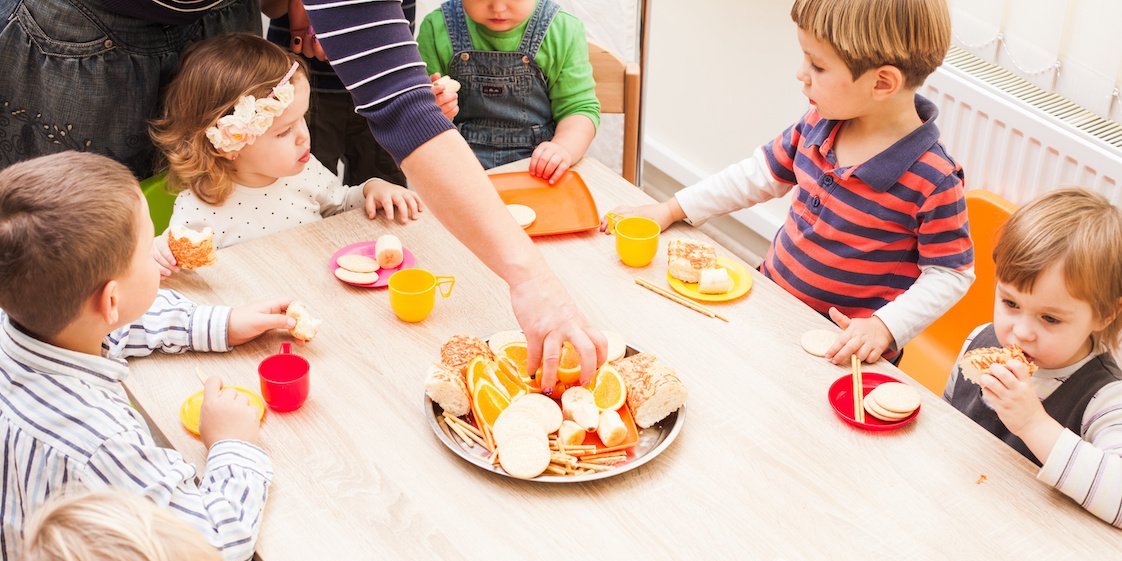 Kitakinder sitzen am Tisch und essen aufgeschnittenes Obst als Nachmittagsimbiss.. Artikel "Ernährungsbildung im Alltag fördern" öffnen.