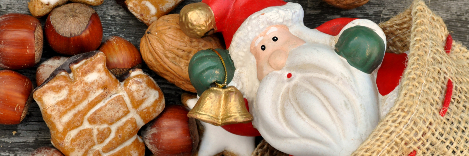 Eine Nikolausfigur schaut aus einem Jutesack hervor. Darum liegen Walnüsse und Haselnüsse sowie Weihnachtsgebäck.  