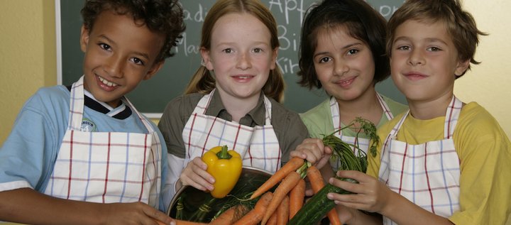 Vier Kinder mit Küchenschürze und Gemüse