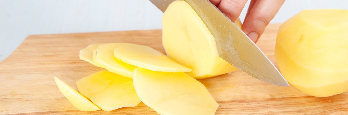 Person schneidet rohe Kartoffel mit Messer in Scheiben.