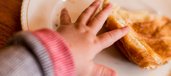 Hand eines Babys greift nach Croissant auf Teller.
