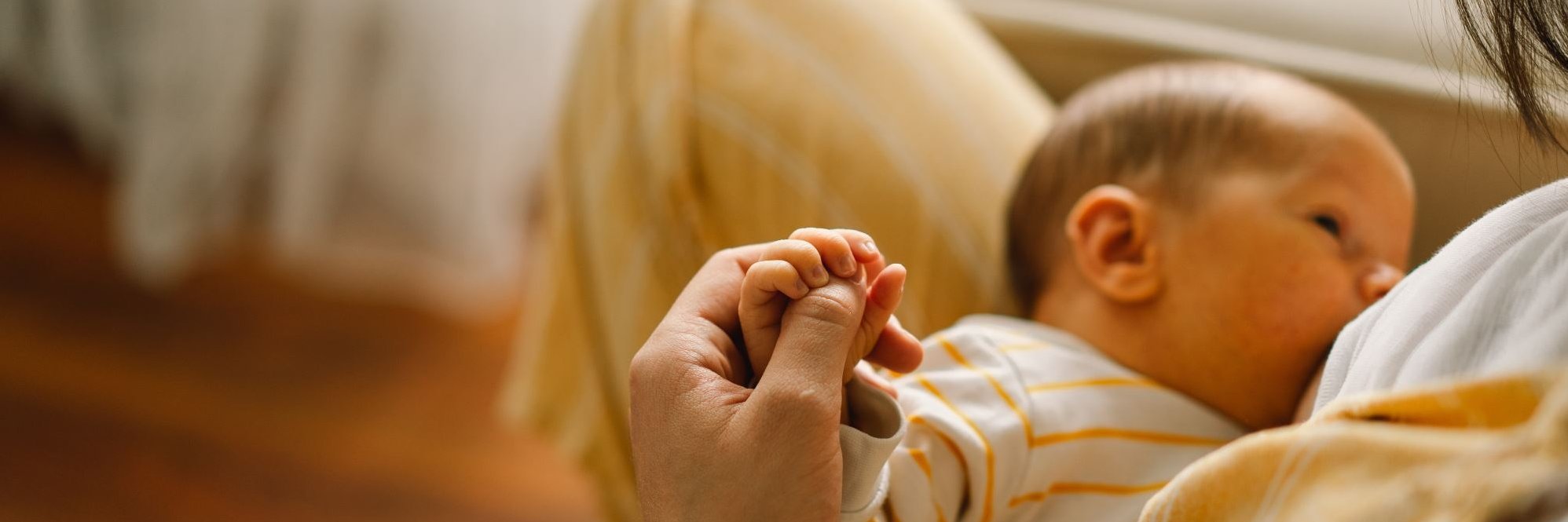 Ein Baby liegt an der Brust der Mutter. Die Mutter hält die Hand des Babys.