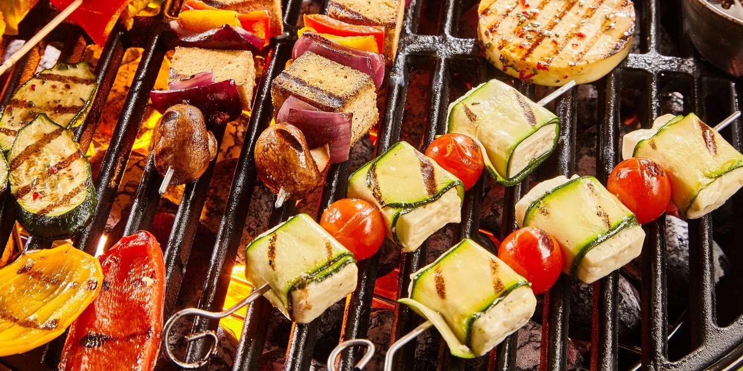Auf einem Grillrost liegen verschiedene Spieße mit Zwiebeln, Zucchinistreifen, Fetawürfeln und Cocktailtomaten sowie einzelne Paprikastücke.  . Artikel "Ruckzuck Grillideen für den Feierabend" öffnen.
