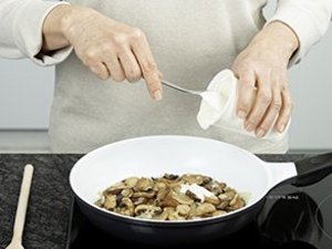 Eine Person gibt saure Sahne in Pilzpfanne.