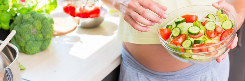 Eine schwangere Frau hält eine Schüssel mit Salat in den Händen.