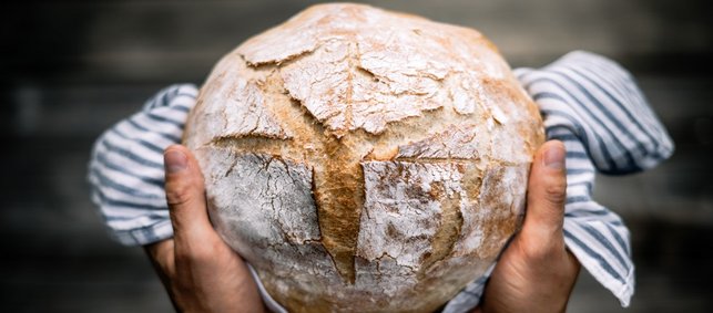 Ein rundes Brot wir in einem Küchentuch eingeschlagen päsentiert.