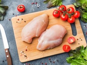 Zwei rohe Stücke Fleisch liegen zusammen mit Tomaten und Salatbrlättern auf einem Schneidebrett.