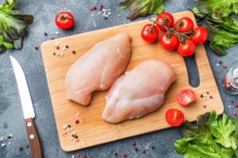 Zwei rohe Stücke Fleisch liegen zusammen mit Tomaten und Salatbrlättern auf einem Schneidebrett.