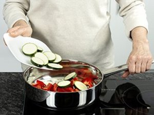 Eine Person gibt Zucchinischeiben und Paprika in einen Topf.