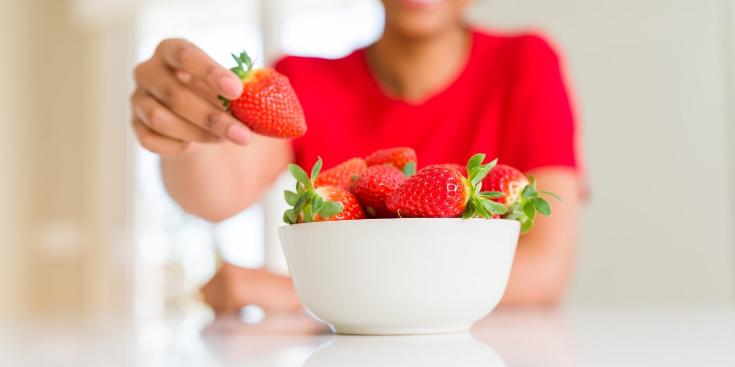 Eine Frau mit rotem Pulli greift aus dem Hintergrund in eine Schale mit frischen Erdbeeren.