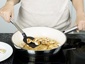 Eine Person brät Hähnchenstücke in Pfanne.