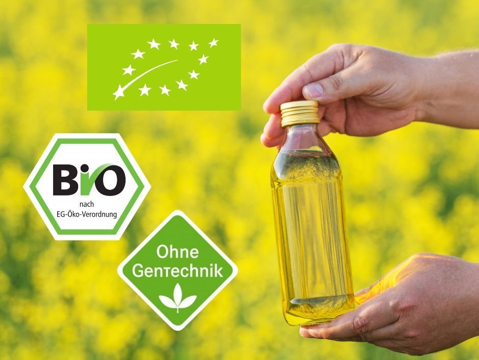 Eine Hand hält eine kleine Glasflasche mit Rapsöl vor einem Rapsfeld. Daneben sind das EU-Bio-Logo, das staatliche Bio-Siegel und das  „Ohne Gentechnik“-Label platziert.