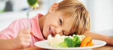 kleiner Junge sitzt vor einem Teller mit Gemüse