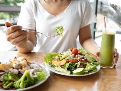 Eine Person nimmt eine pflanzliche Mahlzeit ein. Auf dem Teller ist ein großer Salat und daneben steht ein grüner Smoothie.