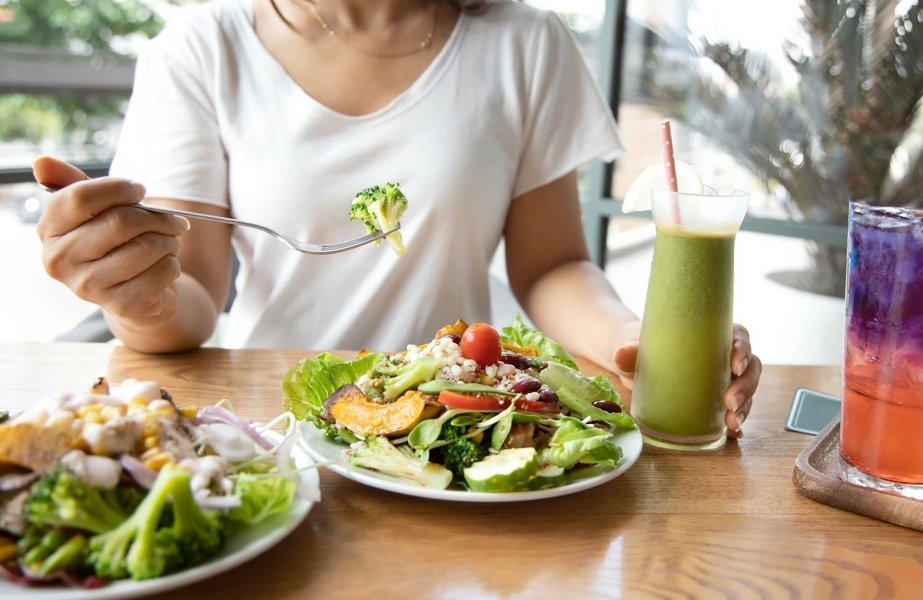 Eine Person nimmt eine pflanzliche Mahlzeit ein. Auf dem Teller ist ein großer Salat und daneben steht ein grüner Smoothie.