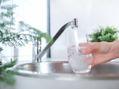 Eine Hand füllt ein Glas mit Wasseraus dem Wasserhahn.