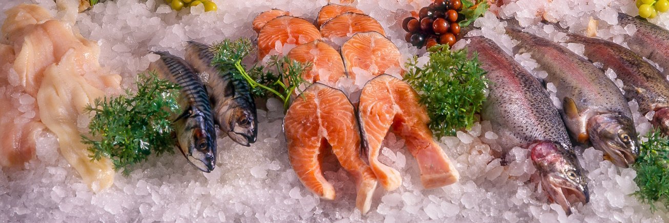 Verschiedene ganze Fische und Fischfilets liegen in einer Theke auf viel Eis.