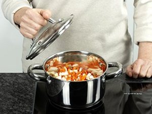 Person dünstet Sellerie und Möhren in einem Kochtopf.